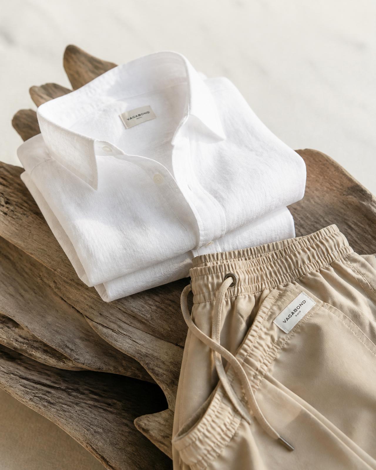 Folded white linen shirt and sand-colored swim shorts on weathered driftwood