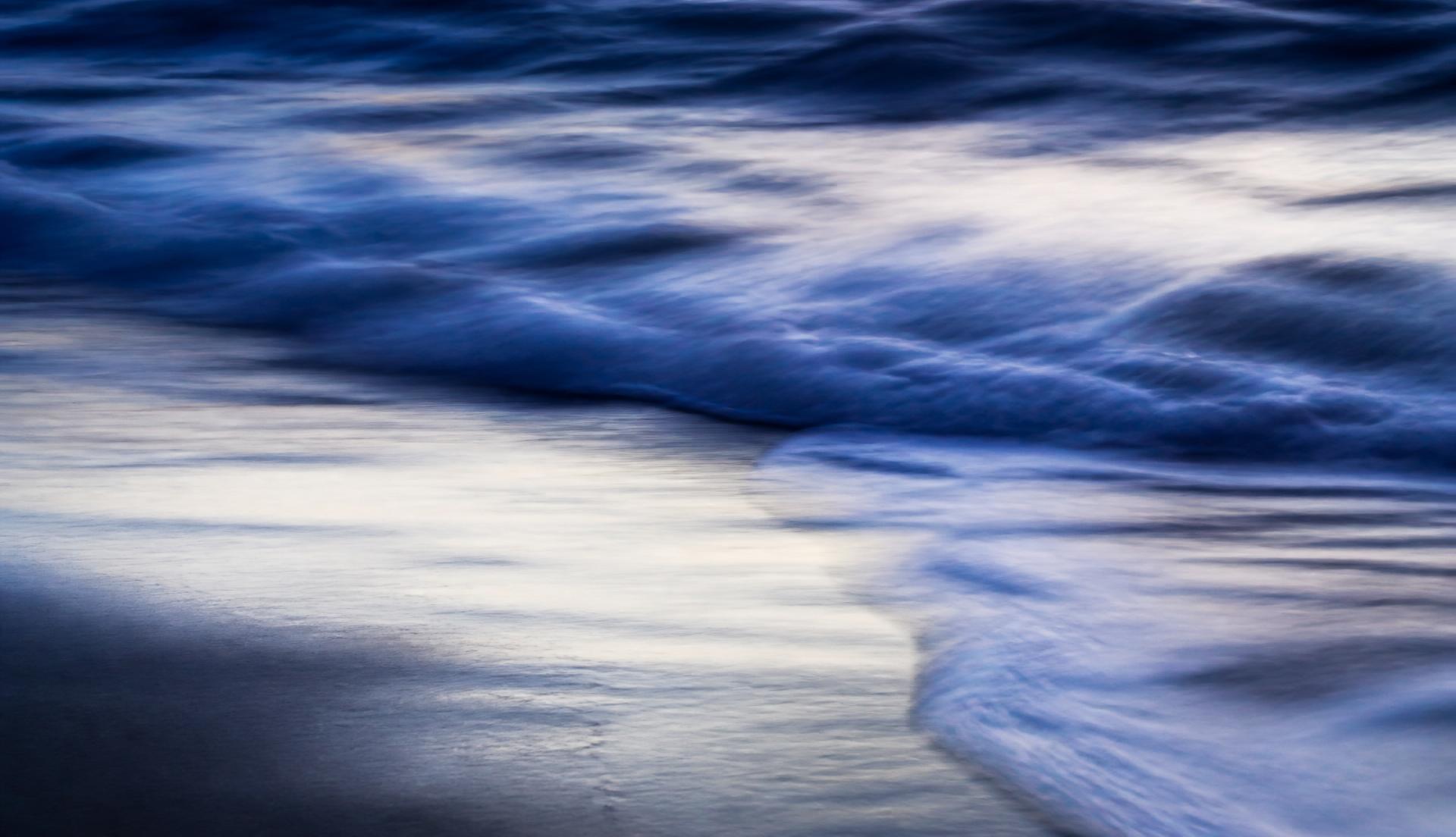 Long exposure waves washing over white sand at dusk